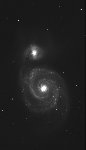 Black-and-white image of the spiral galaxy M51, also known as the Whirlpool Galaxy, taken through a red filter. The galaxy displays a bright core with distinct spiral arms winding outward, dotted with stars and bright regions. A smaller companion galaxy is visible near the top, connected by a faint bridge of material