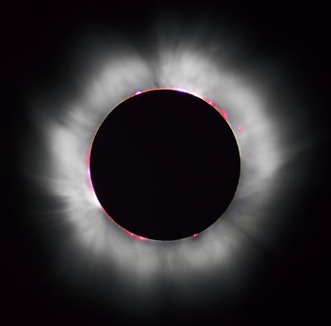 Image of a total solar eclipse showing the Sun's corona and solar prominences around the Moon's silhouette during totality