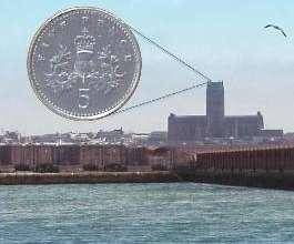 An image of a coastline with a large coin magnified over a distant cathedral, demonstrating perspective or scale