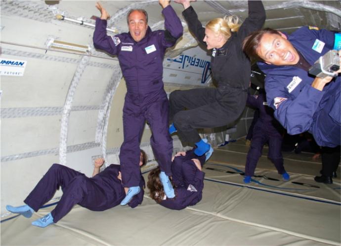 Several people in flight suits experiencing weightlessness inside a plane during a zero-gravity flight, floating and smiling as they enjoy the sensation of floating in mid-air.